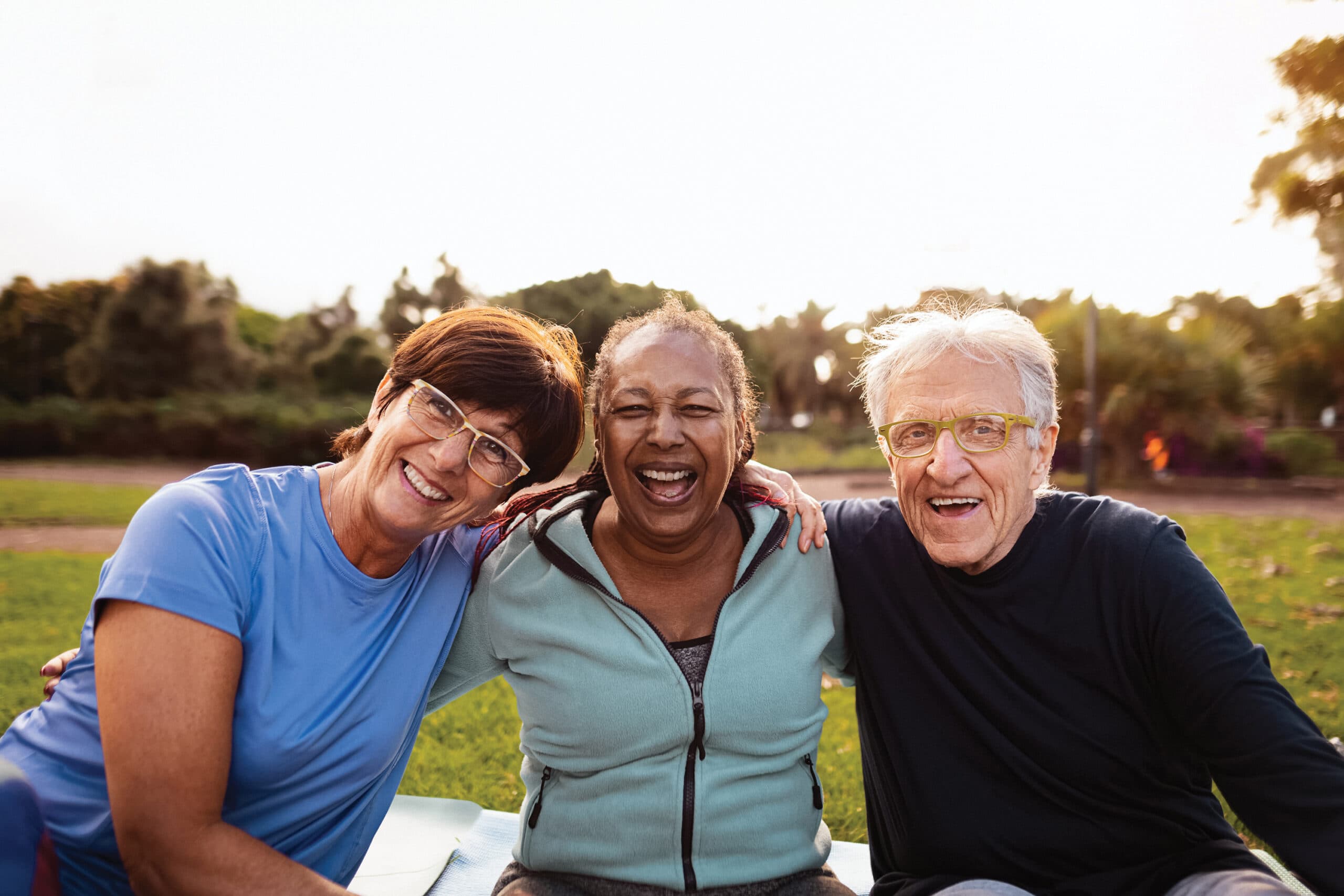 Three friends smile for the camera as they sit in a park.
