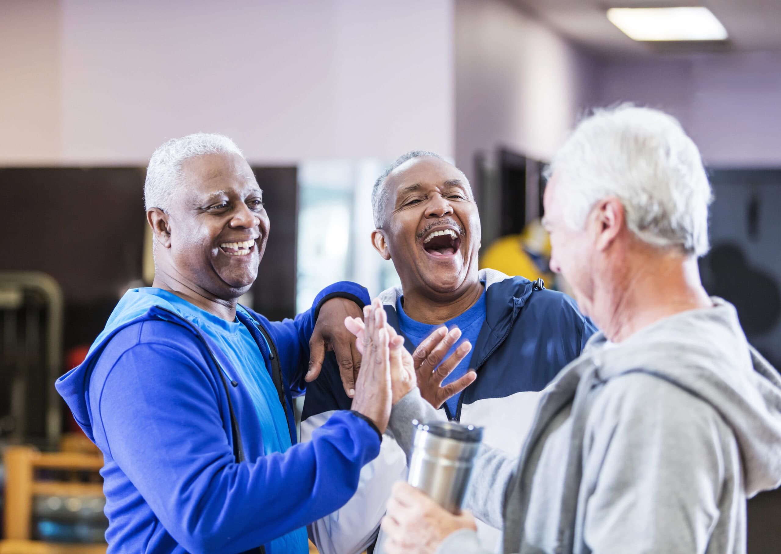 Three older men hang out and talk at the gym.